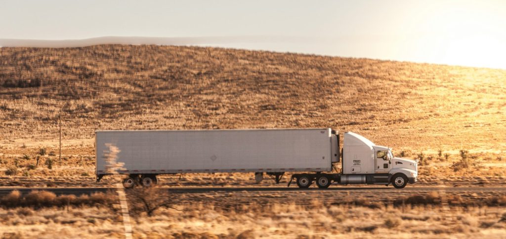 a white semi truck driving down a rural road